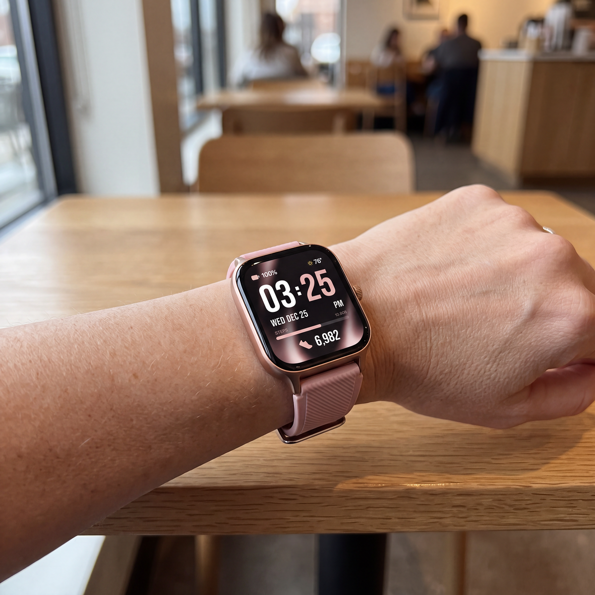 A smartwatch with a vintage rose band and rose gold-toned case worn on a person's wrist, resting on a light wood table in a blurred cafe setting.

Details